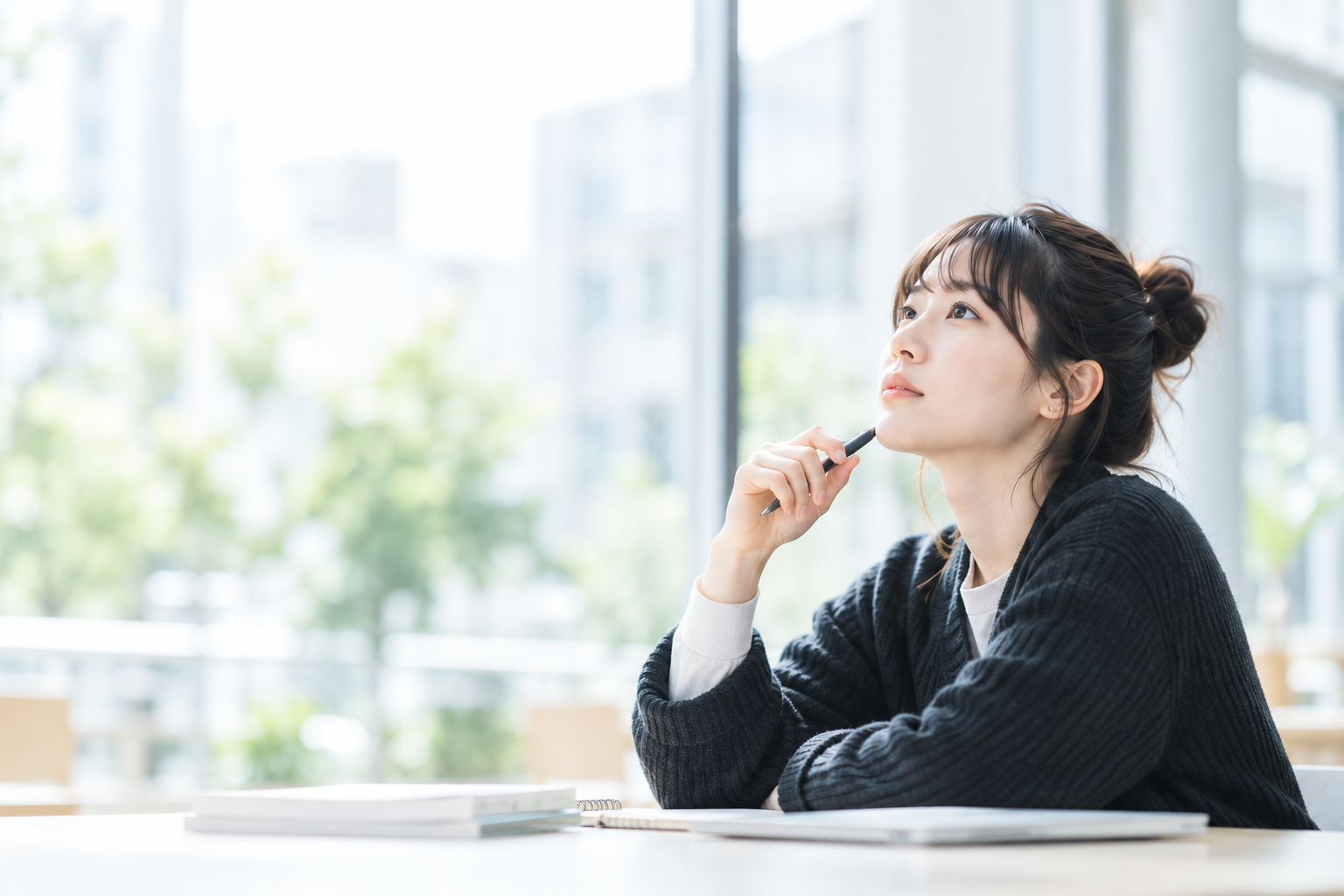 明るい窓辺でペンを手に考える学生のイメージ（AI生成）